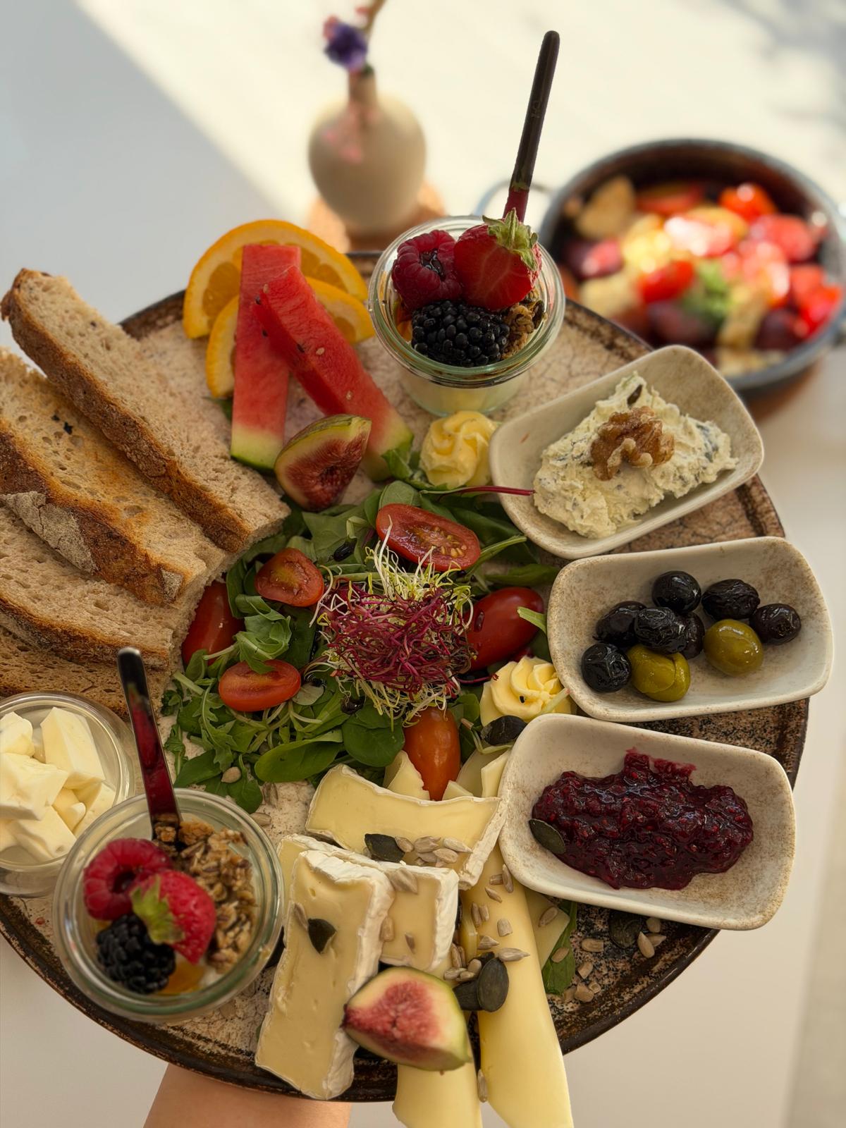 Reichhaltige Frühstücksplatte mit Brot, Käse, Oliven und frischen Früchten
